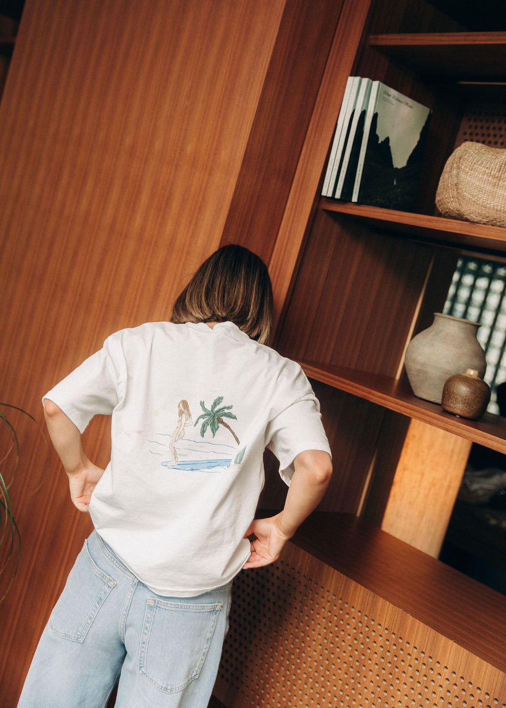 Model wearing the white Surfer Girl Tee with Seven Wellness Club on the front, boxy fit